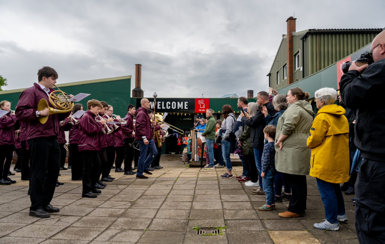 Group of visitors watch a brass band play in front of a musuem
