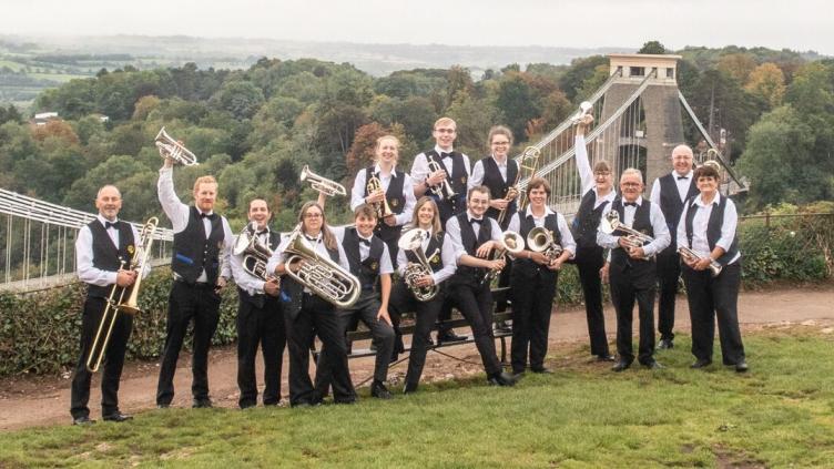 A group of people wearing matching black and white uniforms holding brass instruments standing on a grass field