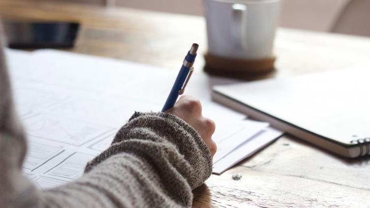 A person writing a letter with a pen